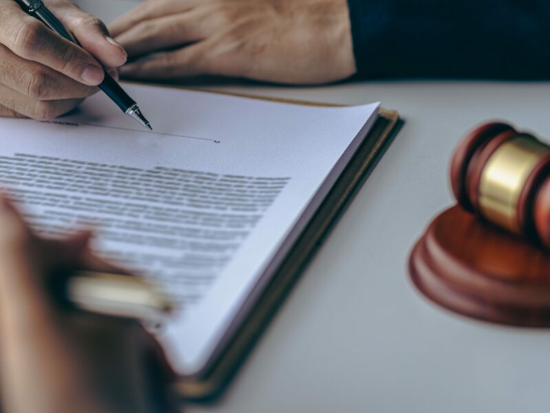 A document is being signed next to a gavel, indicating a legal concept.